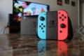 Im Vordergrund ein Nintendo Switch Controler, im Hintergrund eine Nintendo Switch Docking-Station und ein gro&szlig;er Bildschirm