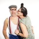 skeptischer u. hilfesuchender Blick v. Alois; Elsbeth versucht ihm einen Kuss auf die Wange zu geben und zieht dabei an seinem Hosenriemen.