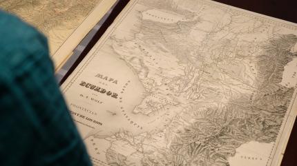 Historische Landkarte von Ecuador mit topografischen Details, auf einem Tisch liegend, im Vordergrund unscharf eine Person in gr&uuml;nem Pullover.