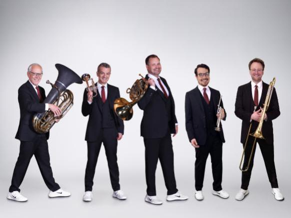 F&uuml;nf Musiker mit Ihren Instrumenten in schwarzen Anz&uuml;gen mit wei&szlig;en Sneakern. Ein Tubist, ein Hornist, zwei Trompeter und ein Posaunist