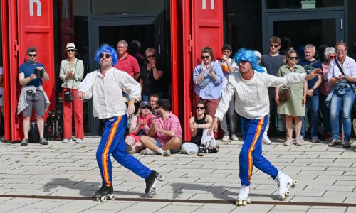 zwei Rollschuhläufer mit blauen Hosen und Helm sowie weissen Oberteil