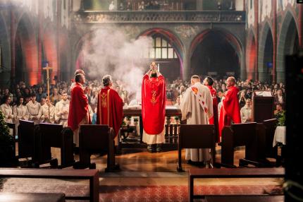 Priester hält Hostie bei der Wandlung vor den Augen der Gemeinde nach oben