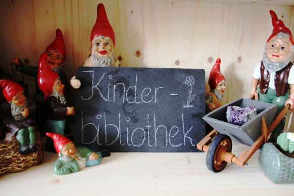 Gruppe von kleinen Gartenzwergen und schwarze Tafel mit Aufschrift Kinderbibliothek