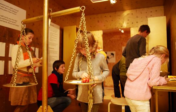 Ein Kind wiegt an einer großen Pendelwaage im Mach-Mit-Bereich im Kindermuseum verschiedene Gegenstände.