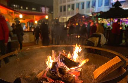 Feuerschale, im Hintergrund Marktstände und Besucher auf dem Weihnachtsmarkt