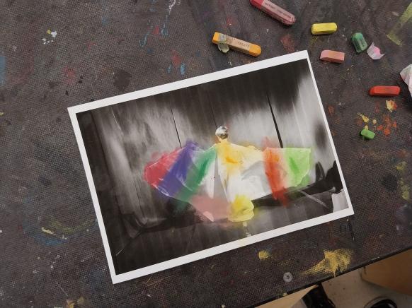 Zu sehen ist eine ausgedruckte Fotografie von einem tanzenden Kind in Umhang mit aufgemalten bunten Zeichnungen.