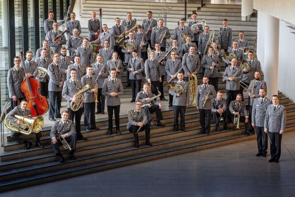 Das Orchester steht versammelt in Uniform und seinen Instrumenten in der Hand im Eingangsbereich, verteilt auf den Treppen, des CCUs.