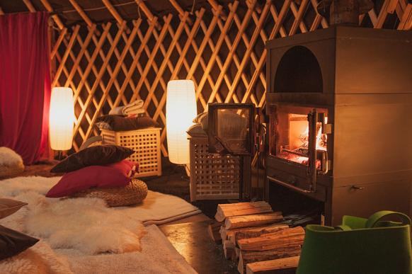 Kaminofen mit Holz davor, kuschelige Decken und eine gemütliche Beleuchtung