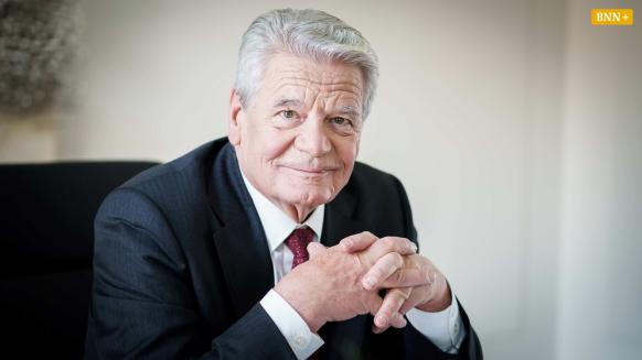 Joachim sitzt an einem Tisch. Blick in die Kamera gerichtet.