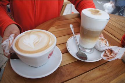 Eine Tasse Cappuccino und ein Latte Macchiato werden auf einem Tisch abgestellt.
