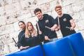 Vier Personen trommeln mit Stöcken auf blaue Holzfässer